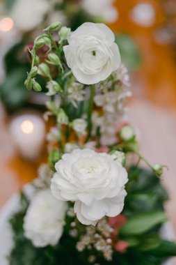 Ranunculus ve narin yeşillikler de dahil olmak üzere taze beyaz çiçekler zarif bir toplantı sırasında ahşap bir masanın üzerindeki büyüleyici bir süslemede düzenlenir..