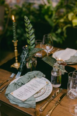 Lezzetli bir yemek masasında güzel yemek takımları, yeşillikler ve mumlar sergileniyor. Arkadaşlar ve aile arasında sıcak bir ortam yaratıyor..