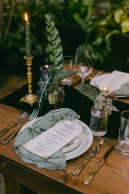 Güzel düzenlenmiş bir yemek masasında hassas cam eşyalar renkli yapraklar ve büyüleyici bir menü sergileniyor. Yumuşak mum ışığı davetkar çevreye sıcaklık katar..