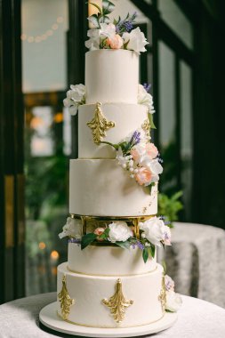 Bu göz kamaştırıcı altı katlı düğün pastası karmaşık altın detaylar içeriyor ve güzel bir şekilde taze çiçeklerle süslenmiş. Zarif bir karşılama ortamının en önemli parçası olarak duruyor..