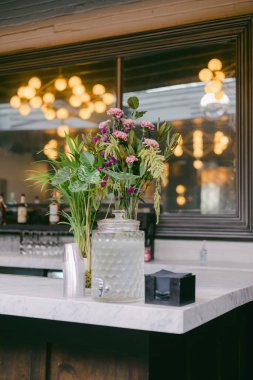 Taze çiçeklerle dolu güzel düzenlenmiş bir vazo cilalı bir tezgahın üzerinde duruyor. Mekanda sıcak bir ışık ve zarif bir atmosfer var. Toplantılar için mükemmel..