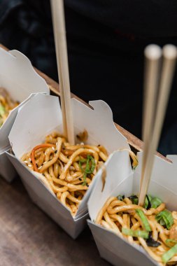 Lezzetli erişteler hazır yemek kutularında sergileniyor, hareketli bir öğleden sonra boyunca yemek çubuklarıyla keyif almaya hazır, canlı bir yemek kültürü sergiliyorlar..