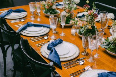 Güzel düzenlenmiş bir masa beyaz tabaklar, mavi peçeteler ve zarif cam eşyalar içerir. Çiçek süslemeleri sofistike atmosferi geliştirir, toplanmak için mükemmeldir..