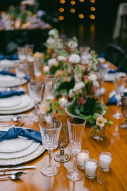 A beautifully arranged dining table showcases floral centerpieces, crystal glasses, and flickering candles, creating a warm ambiance perfect for a celebration or gathering. clipart