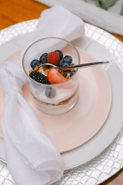 Katmanlı bir tatlı sunumu kremalı yoğurt, granola ve çilek ve yaban mersini gibi çeşitli taze böğürtlenler, el değmemiş bir peçeteyle pastel bir tabağa konur..