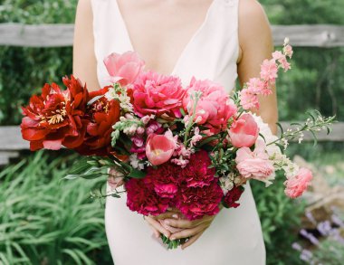 Bir gelin, neşeli bir yaz kutlamasında yemyeşil çiçeklerin arasında canlı bir buket tutar..