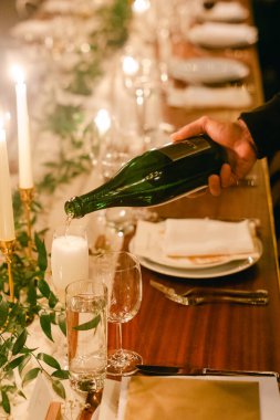 Bir el, şampanyanın içine mumların yanında şampanya döker. Akşam yemeğinin zarafetini arttırır..