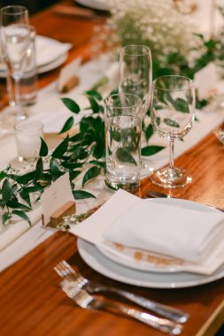 Yeşillik, cam kaplama ve şenlik için düzgünce katlanmış peçetelerle süslenmiş güzel bir yemek masası..