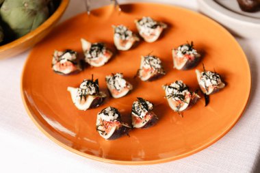 Canlı bir turuncu tabak, otlar ve deniz ürünleriyle süslenmiş bir dizi iyi hazırlanmış kanepe sergiliyor. Dekorasyon, davetlileri şenlikli bir aşçılık etkinliğine davet ediyor..