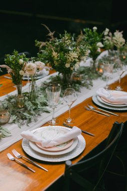 Zarif sofra takımları, kristal bardaklar ve taze çiçek süslemeleri olan güzel düzenlenmiş bir yemek masası. Yumuşak ışıklandırma misafirler için davetkar bir ortam yaratır..