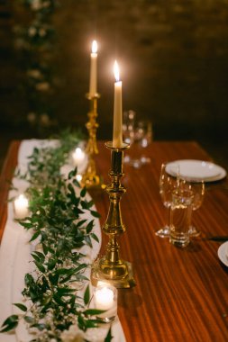 Zarif masa düzeninde mum, yeşillik ve loş ışık yemek için romantik bir ortam yaratıyor..