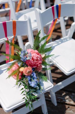 Canlı bir çiçek ve yeşillik düzeni bahar boyunca bir açık hava düğününde beyaz bir sandalyeyi vurguluyor..