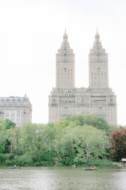 İnsanlar, Central Park 'ta bulutlu gökyüzünün altında ağaçlarla ve ikiz kulelerle çevrili sakin bir gölde kayıkla gezmekten hoşlanırlar..