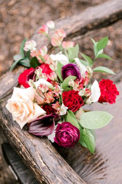 Kırmızı, beyaz ve mor çiçeklerden oluşan canlı bir buket bahçedeki doğal ahşap bir bankta duruyor..
