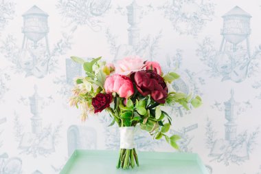 Taze yeşillikle pembe ve bordo güller içeren canlı bir buket, dekoratif bir arka planda..