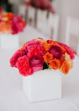 Pembe ve turuncu renkli canlı bir çiçek koleksiyonu kutlama için sofra düzenini güçlendirir..