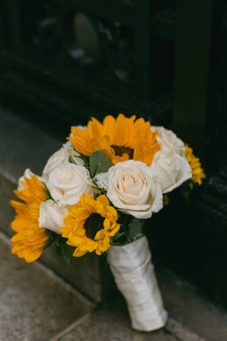 Canlı bir ayçiçeği buketi ve beyaz güller koyu bir yüzeye uzanır, renkleri ve dokuları sergilenir..