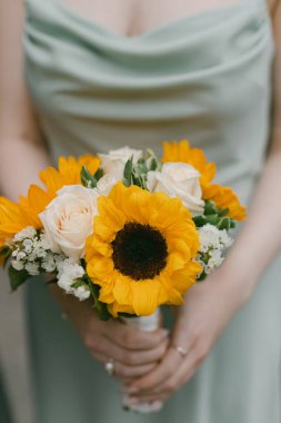 Bir buket ayçiçeği ve gül, neşeli bir etkinlik sırasında yeşil elbiseli biri tarafından tutulur..