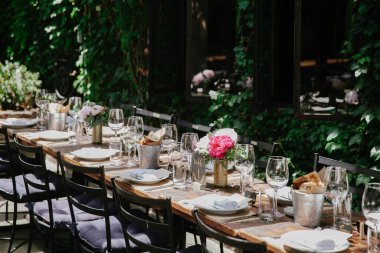 Davetkar bir açık hava masası yemek için güzelce düzenlenir, çiçeklerle süslenir ve yeşilliklerle çevrilidir..