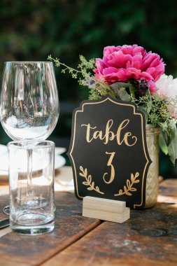 Çok güzel düzenlenmiş bir masada çiçekler, cam eşyalar ve açık hava ortamında büyüleyici bir masa numarası vardır..
