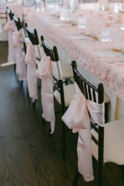 Şenlik için mükemmel bir ziyafet masasının yanında zarif pembe kurdelelerle süslenmiş sandalyeler..