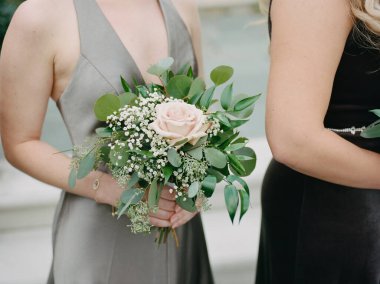 Güzel bir açık hava düğününde nedime elinde taze bir buket pembe gülle zarif bir şekilde duruyor..