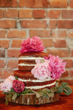 Pembe çiçeklerle süslenmiş üç katlı bir pasta kırsal bir duvarın önündeki tahta bir levhaya konur..