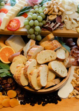 Çeşitli peynirler, pişirilmiş etler, taze meyveler ve dilimlenmiş ekmek kırsal bir ahşap tabakta güzelce düzenlenmiştir..