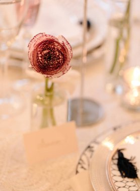 Zarif bir çiçek süsü, pırıl pırıl cam ve şık bir çatal bıçak içeren güzel bir yemek masası..