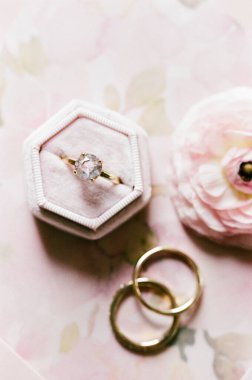 Güzel nişan yüzüğü, yakınlarda alyansları olan, hassas bir pastel arka planda duruyor. Romantik bir tema için mükemmel..