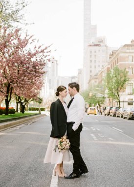 Yeni evli bir çift, güzel bir bahar gününde neşe dolu, kiraz çiçekli bir sokakta kucaklaşır..