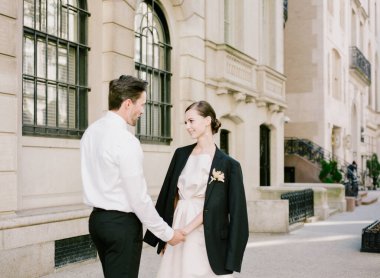 Güzel dizayn edilmiş tarihi bir binanın yanında el ele tutuşurken birbirlerine gülümserler..