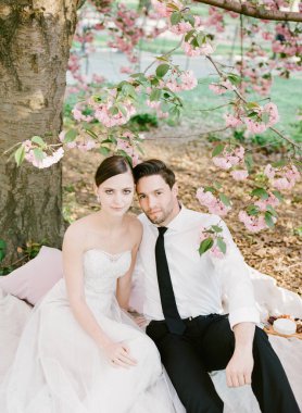 Gelin ve damat, ilkbaharda huzurlu bir anın tadını çıkararak, kiraz çiçekleriyle çevrili bir battaniyenin üzerinde rahatlar..