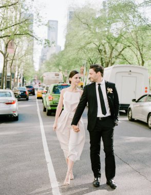 Parlak bir günde yeşil ve şehir trafiği ile çevrili, canlı bir şehir ortamında yeni evliler birlikte yürürler..