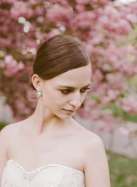 Gelin zarif bir şekilde pembe çiçeklerin arasında duruyor, güzelliğini ve zarafetini mükemmel bir bahar ortamında sergiliyor..