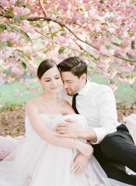 Yeni evli bir çift güneşli bir bahar gününde güzel pembe kiraz çiçekleriyle çevrili huzurlu bir ortamda rahatlar..