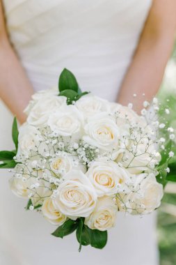 Gelin, romantik bir açık hava düğününde yakalanan beyaz güller ve yeşillikler sergiliyor..