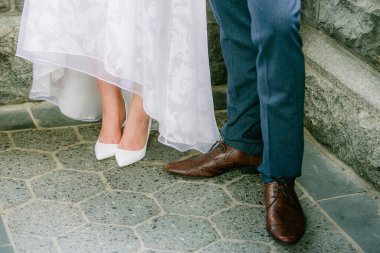 Gelin ve damat birlikte dururlar, zarif ayakkabıları açık hava ortamında desenli bir taşta sergilenir..