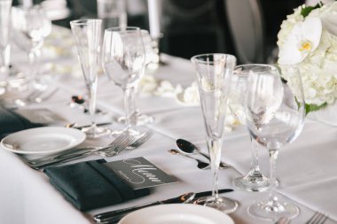 Zarif cam eşyalar, cilalı çatal bıçaklar ve çiçek dekoru olan resmi bir etkinlik için rafine bir masa hazırlanır..