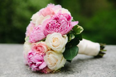 Pembe şakayık ve beyaz güllerden oluşan çarpıcı bir buket, yemyeşil yeşil bir taşın üzerinde durmaktadır..