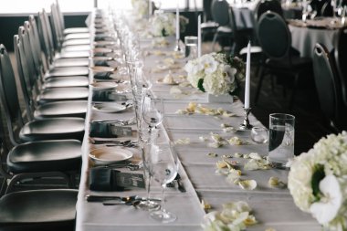 Beyaz çiçekler, mumlar ve zarif sofra takımlarıyla süslenmiş uzun yemek masası düğün kutlaması için hazır..