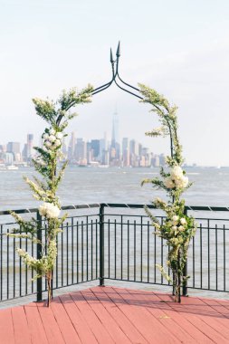 Su kenarındaki güvertede güzel bir çiçek kemeri, berrak gökyüzünün altında çarpıcı bir şehir silüeti..