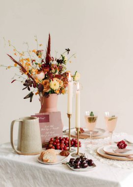 Güzelce hazırlanmış bir masada canlı bir çiçek süsü, içecekler ve bir toplanma için davetkar atıştırmalıklar vardır..