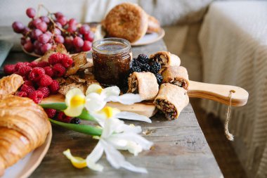Güzel hazırlanmış kahvaltıda hamur işleri, taze meyveler ve ahşap bir yüzeye konmuş bir kavanoz reçel vardır..