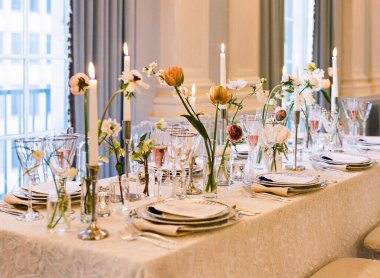 Çok güzel düzenlenmiş bir yemek masasında çiçekler ve mumlar konuklara cazip bir ortam yaratıyor..