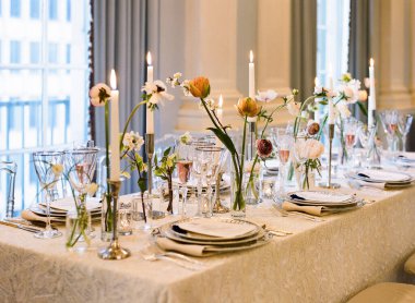 Güzelce hazırlanmış masa vitrinleri, cam süsler ve çiçek aranjmanları, misafirler için sofistike bir atmosfer yaratıyor..