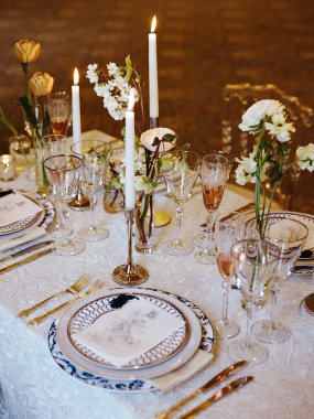 Çok güzel düzenlenmiş bir yemek masasında özel durumlar için mumlar, çiçekler ve zarif sofra takımı bulunur..