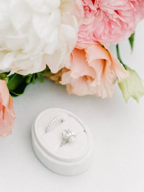 Nişan yüzüğü, sıcak ve davetkar bir ortamda pembe ve beyaz çiçeklerin yanında kadife bir yastığın üzerinde duruyor..