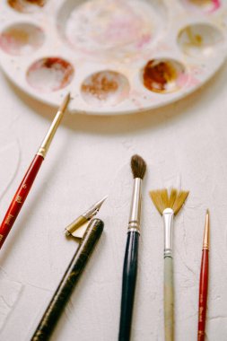 Renkli bir paletin yanında çeşitli boya fırçaları ve aletler bir el sanatları masasında kullanılmaya hazırdır..