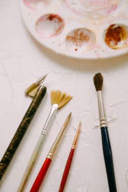 Boya fırçaları ve araçlar düzgün bir şekilde düzenlenmiştir, hafif desenli bir arka planda sanatsal yaratım için hazırlanırlar.